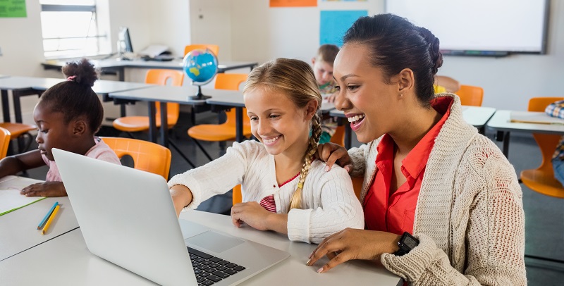 Teacher helping pupil with laptop